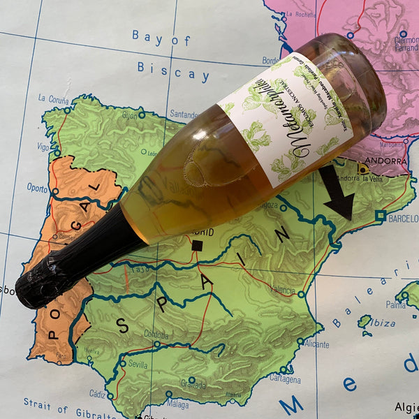 2015 Metamorphika Escumós Ancestral fra Costador i Tarragona, Spanien  Uden tilsat svovl. Vinflasken med en hvid etikette hvor der er grønne sommerfugle på. Vinflasken ligger på et gammelt Europa kort, med en pil der peger på området Tarragona, i Spanien.